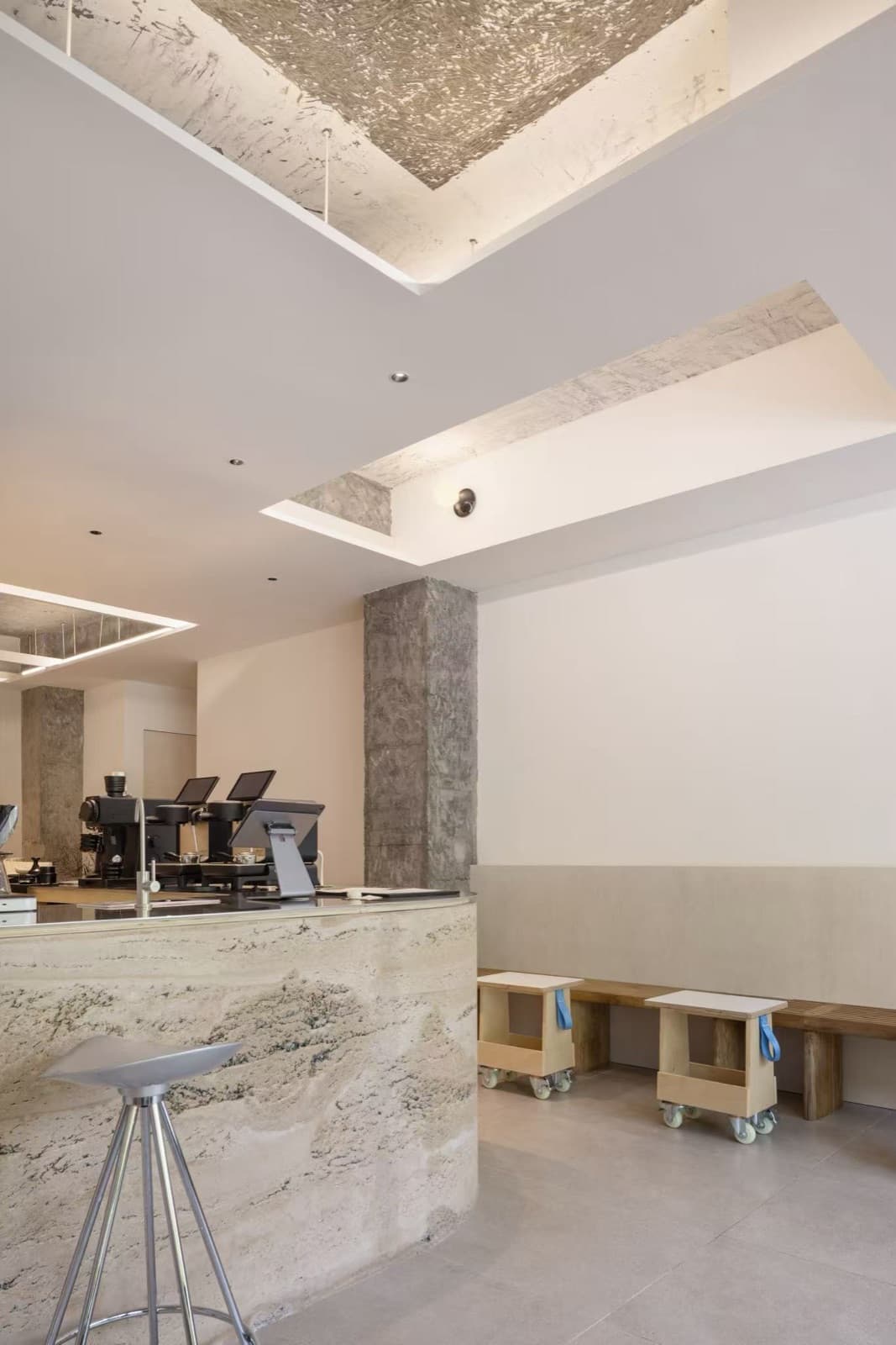 The corner of the bar and a metal stool, espresso machines behind, the bench and stools on the right