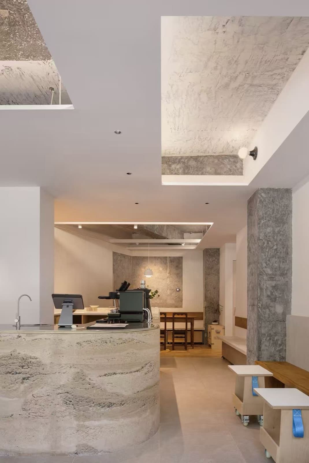 The curved cast bar with the espresso machine and the far long table behind, a concrete column and stools on castors on the right