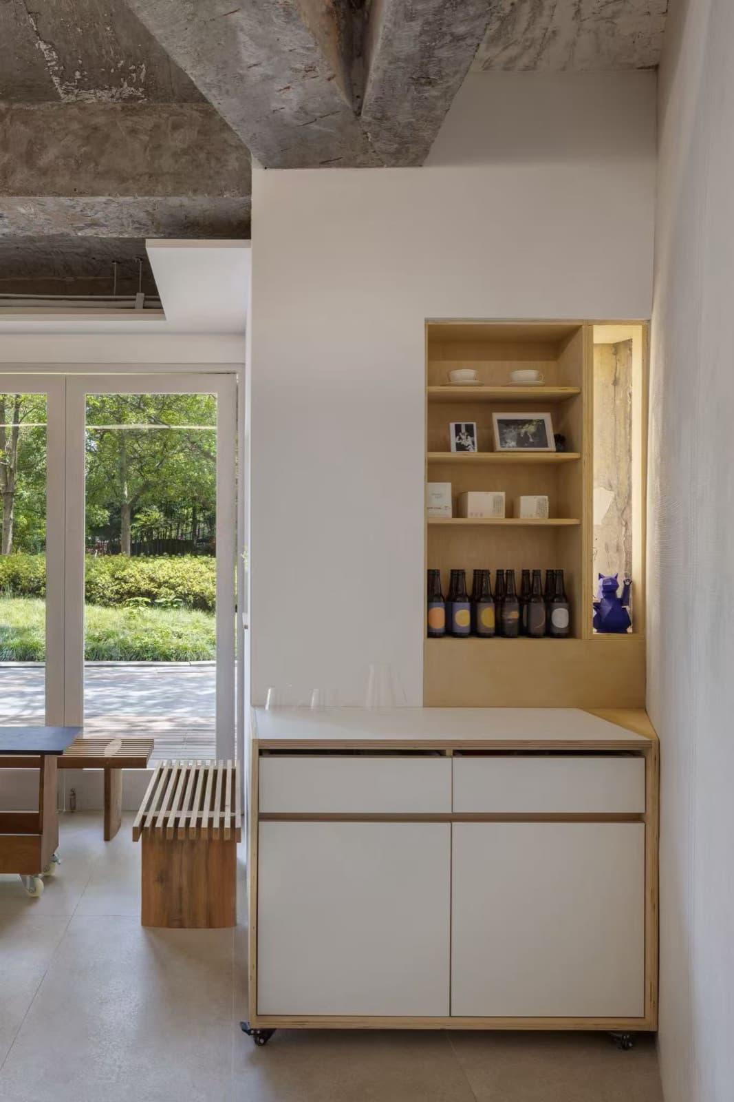 A white cabinet on castors with an oak niche holding bottles, glass doors and the garden behind