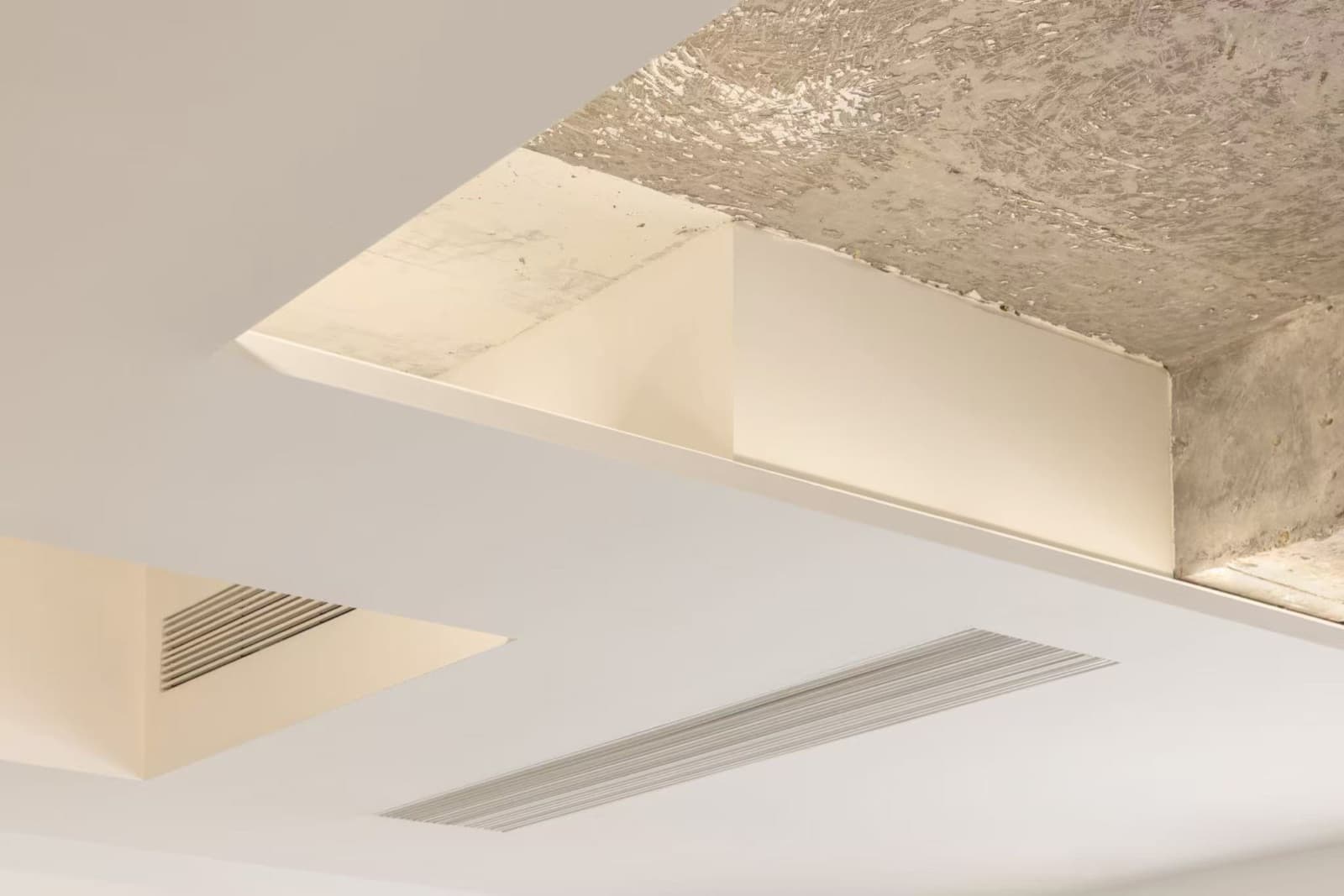 An opening in the white ceiling with a hidden light strip, revealing chiselled concrete