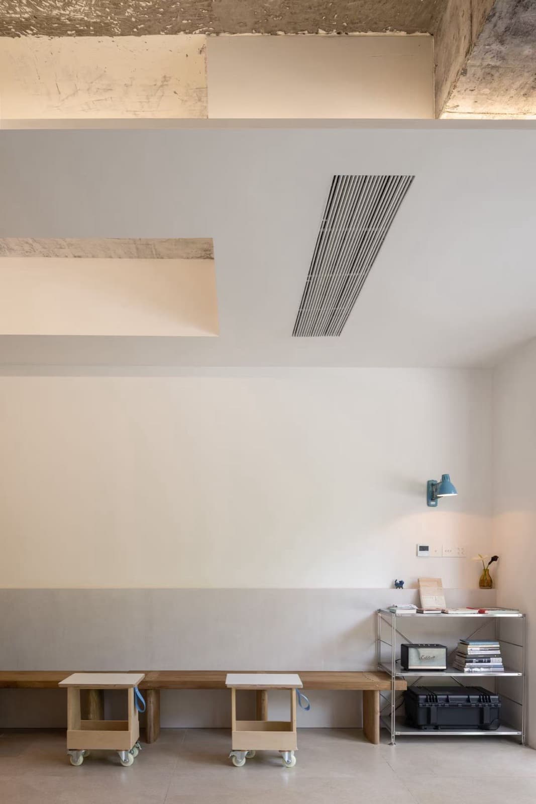 Openings in the white ceiling showing raw concrete, with the wall bench and steel shelf below
