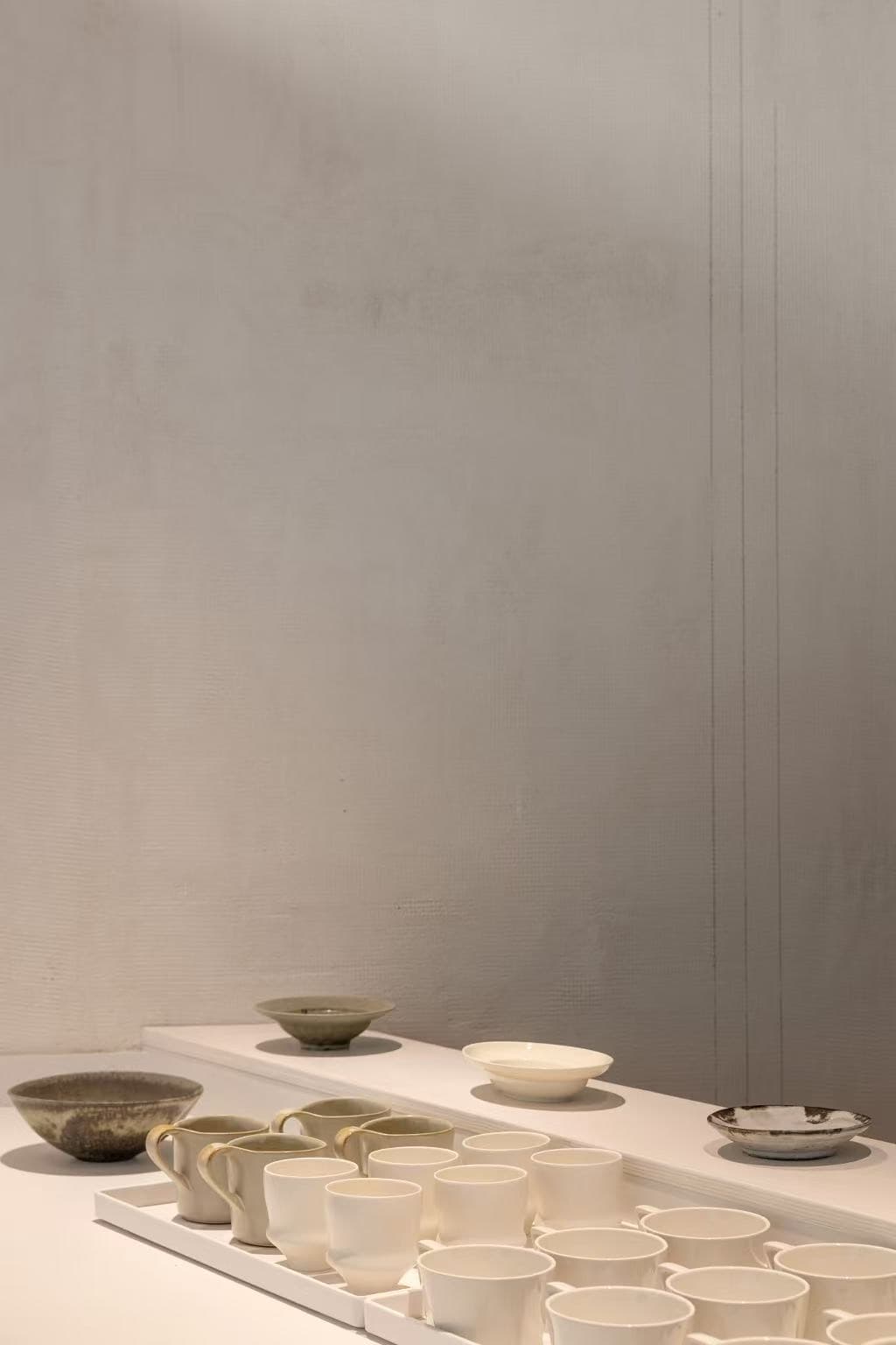 Ceramic bowls and a tray of white cups on a white counter against a grey wall