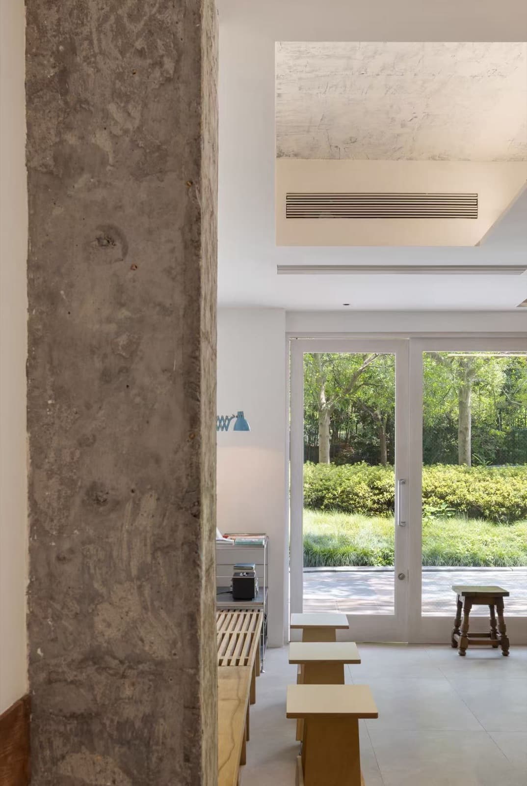 A rough concrete column up close, the glass door onto the garden beyond