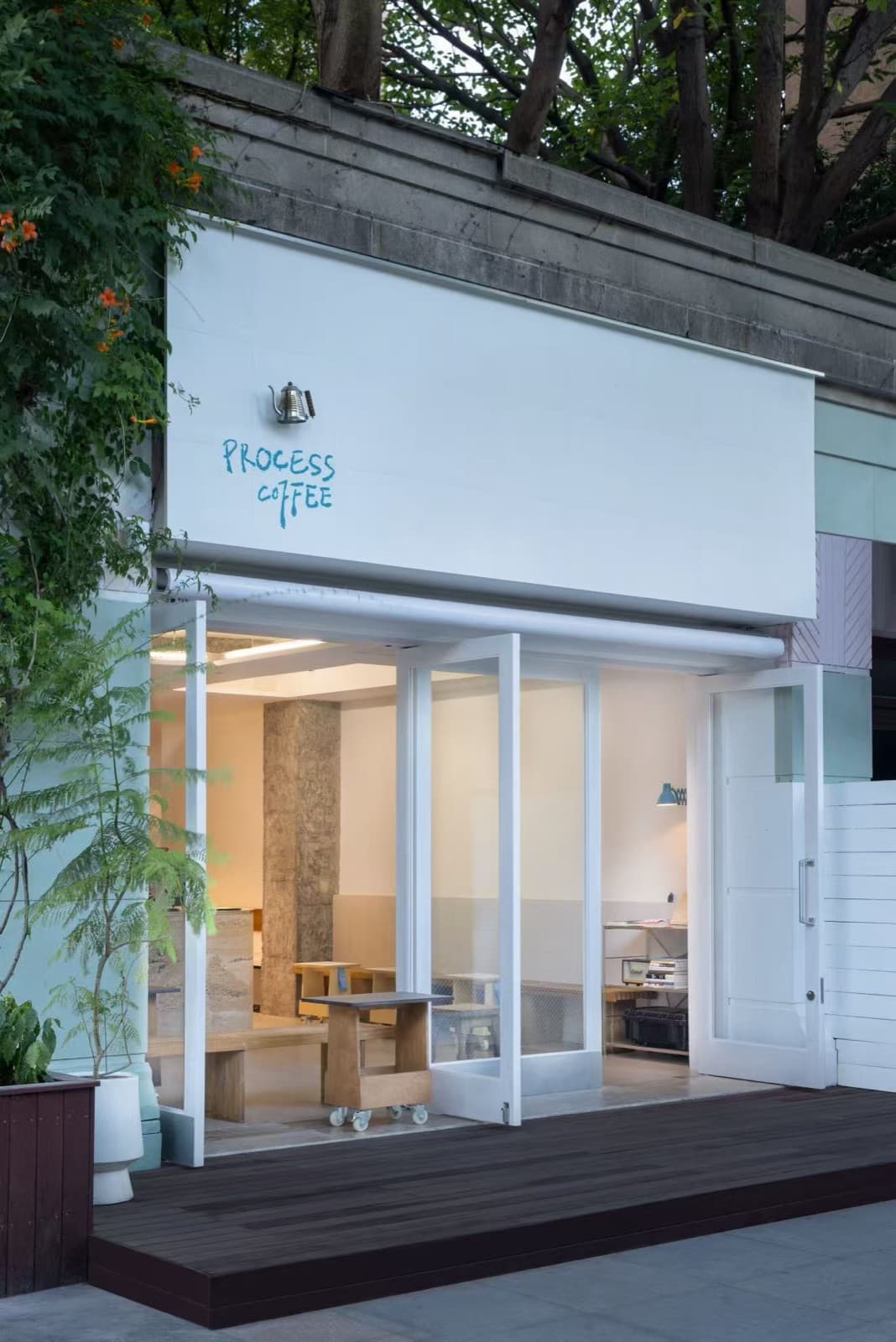 The shopfront at an angle: white sign, open glass doors, the wooden deck and a white planter