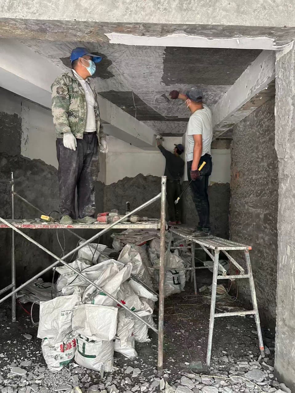 脚手架上的工人在拆旧的吊顶,地上堆着装满碎料的袋子