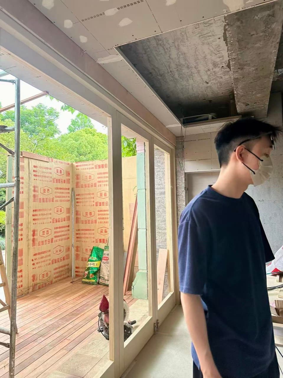一个人站在落地窗边,窗外是铺好的木平台和还没拆的围挡