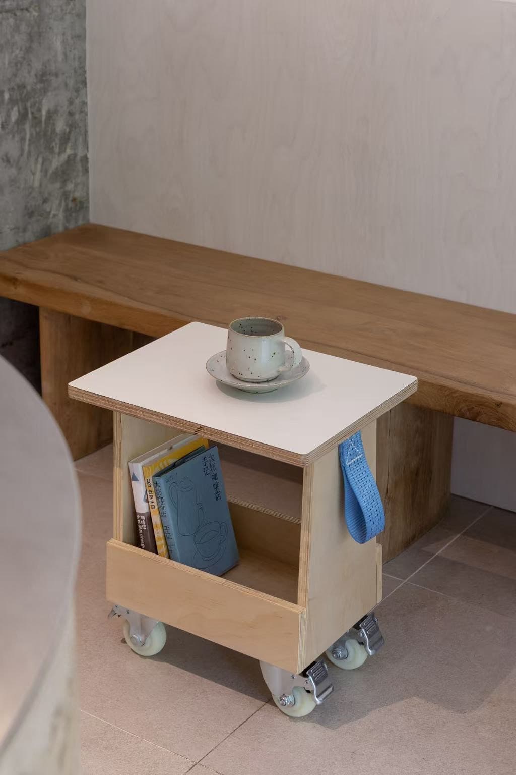 A plywood stool on castors beside the bench, a cup of coffee on top and books underneath