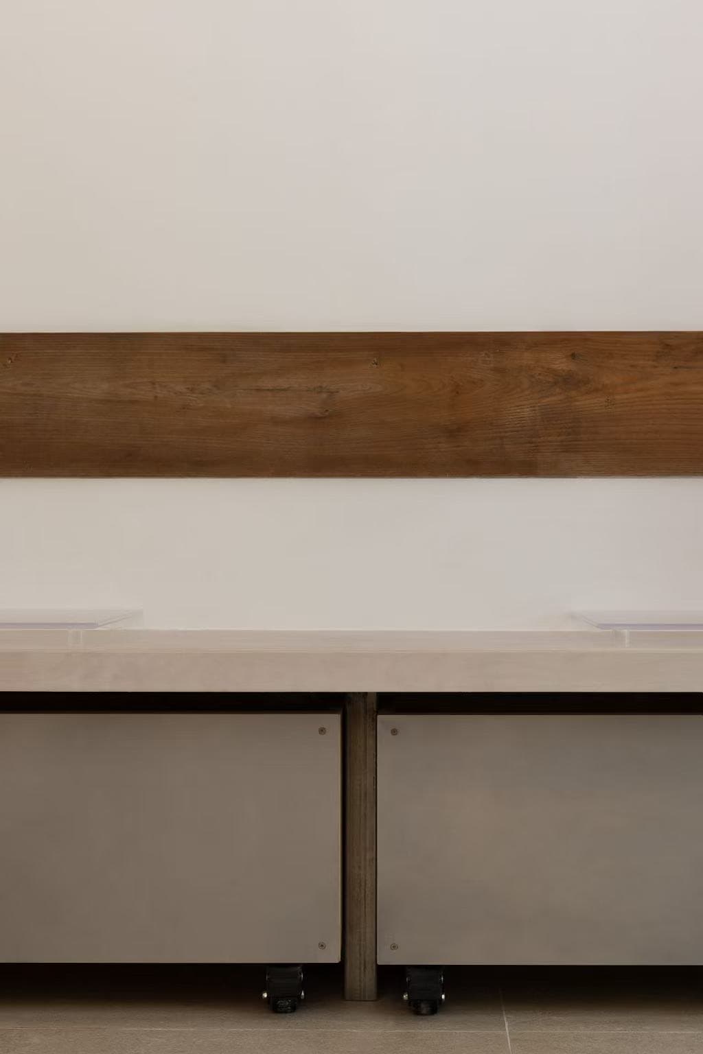 A walnut strip on a white wall above a white-topped bench and two grey cabinets on castors